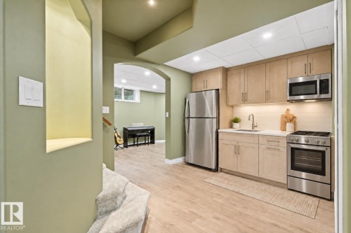 Compact kitchen featuring stainless steel appliances, light wood-finish cabinetry, a white countertop, and tile backsplash - 703 107A Street Sw, Edmonton, AB 