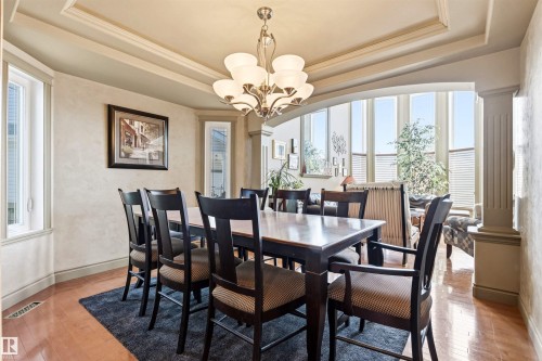 Dining area featuring a tray ceiling with crown molding, a brass chandelier, and wood-finish flooring - 703 107A Street Sw, Edmonton, AB 