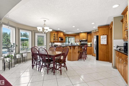 Open-concept kitchen and dining area featuring light-toned wood cabinetry, black countertops, and a full suite of kitchen appliances - 703 107A Street Sw, Edmonton, AB 