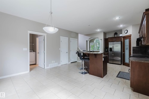 Tile flooring, kitchen island with breakfast bar, wood cabinetry, stainless steel refrigerator, and recessed lighting - 11608 96 Street Nw, Edmonton, AB 