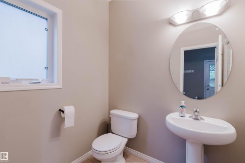 Pedestal sink with chrome faucet, oval mirror, wall-mounted light fixture, and white window frame - 11608 96 Street Nw, Edmonton, AB 