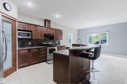 Open-concept kitchen featuring dark wood-finish cabinetry, stainless steel appliances, a stone-finish countertop island with seating, and tile flooring - 