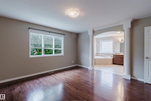 Dark wood-finish flooring with an arched entryway leading to an attached bathroom - 11608 96 Street Nw, Edmonton, AB 