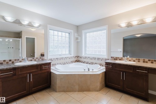 Dual vanity sinks, corner soaking tub, tile flooring, glass block windows, and a tiled shower enclosure - 11608 96 Street Nw, Edmonton, AB 