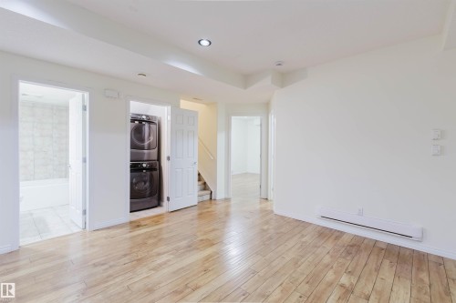 Wood-finish flooring, recessed ceiling lighting, stacked washer and dryer, and a tiled bathroom with a tub - 11608 96 Street Nw, Edmonton, AB 