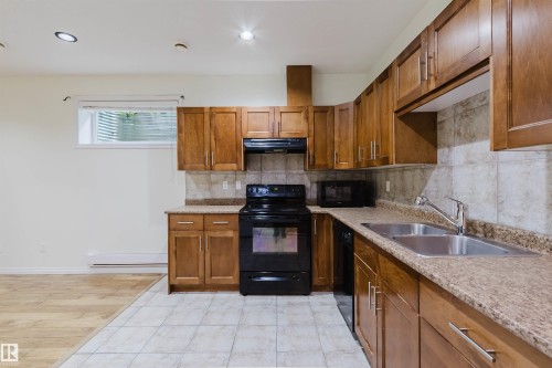 U-shaped kitchen featuring wood cabinetry, stone-look countertops, tile backsplash, and stainless steel double basin sink - 11608 96 Street Nw, Edmonton, AB 