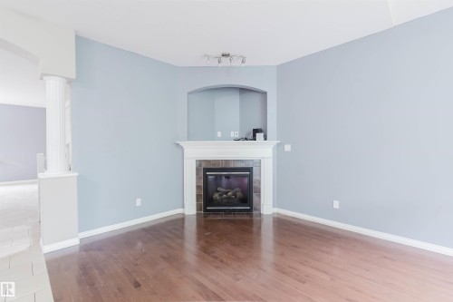 Wood-finish flooring, corner fireplace with tile surround, white mantel, arched wall niche, and track lighting - 11608 96 Street Nw, Edmonton, AB 