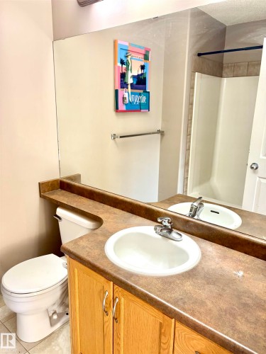 Bathroom featuring a built-in wood-finish vanity with a single basin, an integrated countertop, and a full-width mirror - #17 16317 64 St Nw, Edmonton, AB 