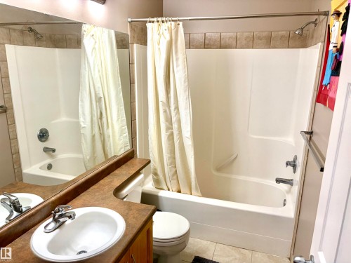 Bathtub and shower combination with a tiled surround, a toilet, a vanity with a surface-mounted sink, and a mirrored wall - #17 16317 64 St Nw, Edmonton, AB 