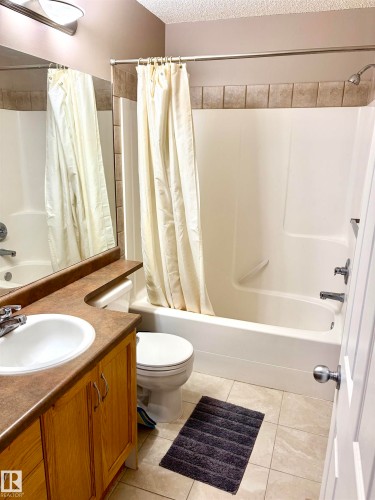 Full bathroom featuring a single vanity with wood-finish cabinetry, a built-in sink, and a combination tub/shower with a tiled accent band - #17 16317 64 St Nw, Edmonton, AB 