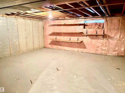 Unfinished lower level featuring exposed ceiling joists, concrete flooring, concrete block walls, and built-in shelving - #17 16317 64 St Nw, Edmonton, AB 
