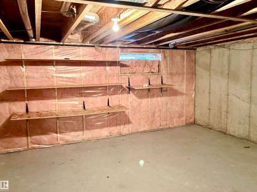 Unfinished basement with concrete flooring, exposed ceiling joists, built-in shelving, and a small window - #17 16317 64 St Nw, Edmonton, AB 