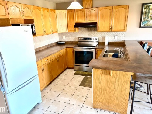 Kitchen featuring wood-finish cabinetry, stainless steel range, white tile backsplash, and a breakfast bar with an integrated sink - #17 16317 64 St Nw, Edmonton, AB 
