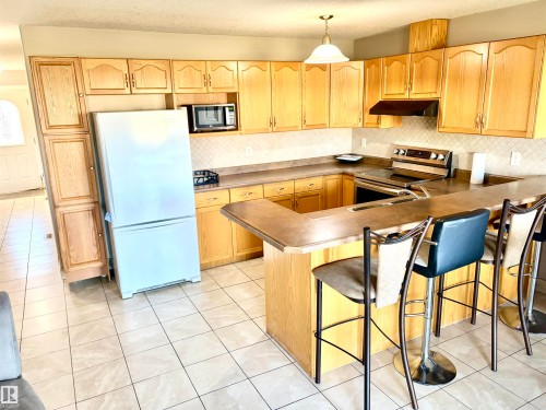 Kitchen featuring extensive light wood cabinetry, a tile backsplash, a built-in oven, a breakfast bar, and tile flooring - #17 16317 64 St Nw, Edmonton, AB 