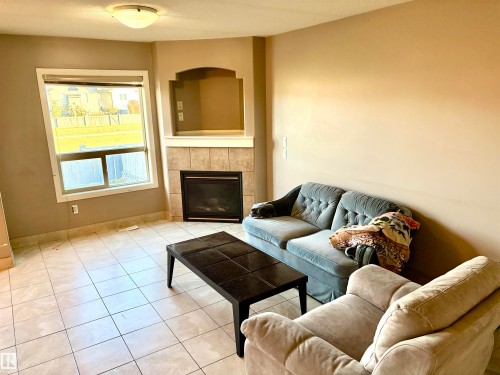Tiled flooring with a corner fireplace featuring a built-in alcove, large window, and ceiling-mounted light fixture - #17 16317 64 St Nw, Edmonton, AB 