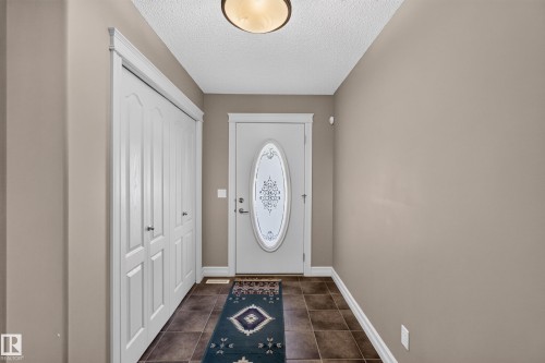 Recessed entryway featuring neutral wall tones, square tile flooring, a built-in closet with bi-fold doors, and a decorative front door with an oval-shaped glass insert - 1850 Rutherford Road Sw, Edmonton, AB 