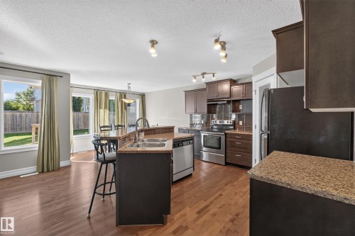 Kitchen featuring wood-finish flooring, dark wood cabinetry, stainless steel appliances, and a kitchen island with sink and seating - 1850 Rutherford Road Sw, Edmonton, AB 