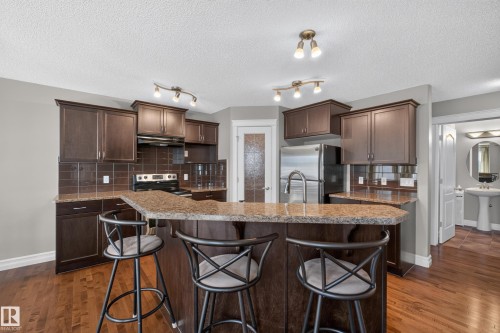 Dark wood-finish cabinetry with granite-style countertops, stainless steel appliances, and wood-finish flooring - 1850 Rutherford Road Sw, Edmonton, AB 