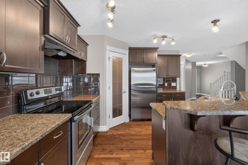 Kitchen featuring dark wood-finish cabinetry, stainless steel appliances, speckled stone countertops, and a tile backsplash - 1850 Rutherford Road Sw, Edmonton, AB 