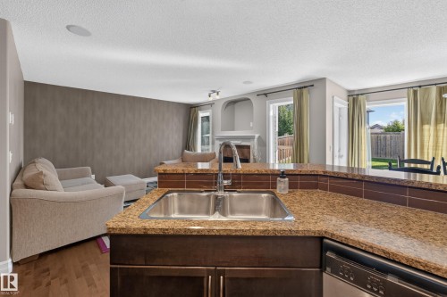 Kitchen featuring a double stainless steel sink, stainless steel dishwasher, and a breakfast bar with stone-look countertops and a tile backsplash - 1850 Rutherford Road Sw, Edmonton, AB 