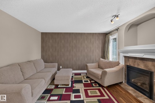 Living area featuring a fireplace with tile surround, a decorative arched niche, track lighting, and wood-finish flooring - 1850 Rutherford Road Sw, Edmonton, AB 