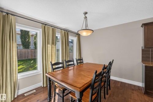 Dining area featuring wood-finish flooring, a contemporary ceiling light fixture, a row of three windows, and a built-in cabinet with a stone-finish countertop - 1850 Rutherford Road Sw, Edmonton, AB 