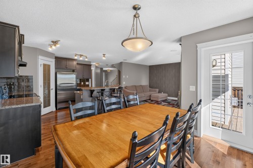 Open concept dining area with wood-finish flooring, a kitchen island with seating, dark wood cabinetry, and a glass-paneled exterior door - 1850 Rutherford Road Sw, Edmonton, AB 