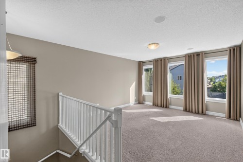 Carpeted upper-level space featuring multiple windows, a white railing, a flush mount light fixture, and recessed ceiling speakers - 1850 Rutherford Road Sw, Edmonton, AB 
