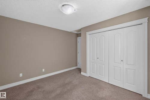 Neutral-toned carpet flooring, textured ceiling, a flush mount ceiling light, and bi-fold closet doors with decorative trim - 1850 Rutherford Road Sw, Edmonton, AB 