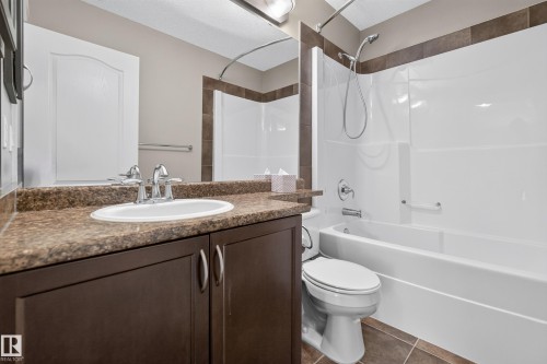 Bathroom featuring a white vanity sink, a patterned countertop, dark wood-finish cabinetry, and a white shower-over-tub unit with a tiled surround accent - 1850 Rutherford Road Sw, Edmonton, AB 