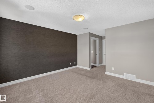 Textured accent wall, neutral carpeting, flush-mount ceiling fixture, recessed ceiling speaker, and white trim - 1850 Rutherford Road Sw, Edmonton, AB 
