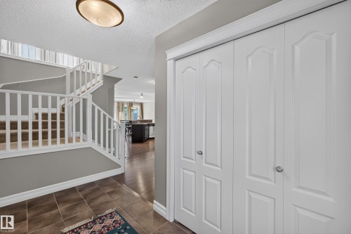 Tiled entryway with overhead flush mount lighting, white bi-fold closet doors, and carpeted stairs with white railings - 1850 Rutherford Road Sw, Edmonton, AB 