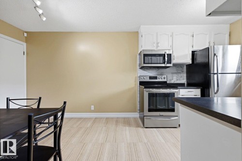 Kitchen featuring stainless steel appliances, white cabinetry, dark countertops, and a tiled backsplash - 11317 22 Avenue Nw, Edmonton, AB 