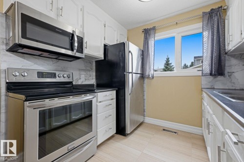 White cabinetry with brushed nickel hardware, light-toned tile flooring, stainless steel appliances, and a marble-finish backsplash - 11317 22 Avenue Nw, Edmonton, AB 