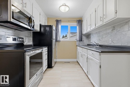 Kitchen featuring white cabinetry, light-colored flooring, stainless steel appliances, and a window - 11317 22 Avenue Nw, Edmonton, AB 