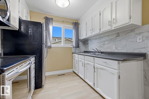 Kitchen featuring white cabinetry, dark countertops, a tile backsplash, and light-toned flooring - 11317 22 Avenue Nw, Edmonton, AB 