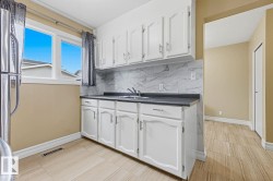 Full white cabinetry, dark countertop, marble-patterned backsplash, light-toned tiled flooring, and a large window - 