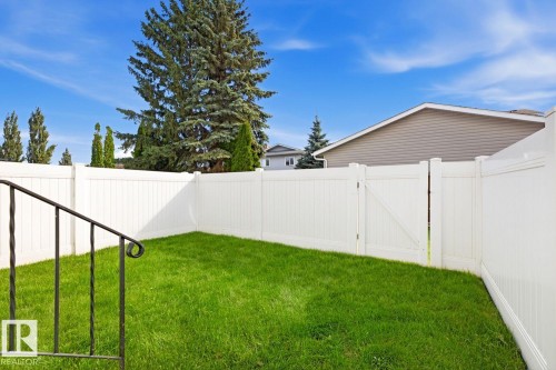 Enclosed backyard featuring a white privacy fence, green lawn, and a gate - 11317 22 Avenue Nw, Edmonton, AB 