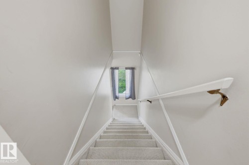 Carpeted staircase with wall-mounted handrail, leading to an upper level with a window - 11317 22 Avenue Nw, Edmonton, AB 