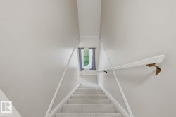 Carpeted staircase with wall-mounted handrail, leading to an upper level with a window - 