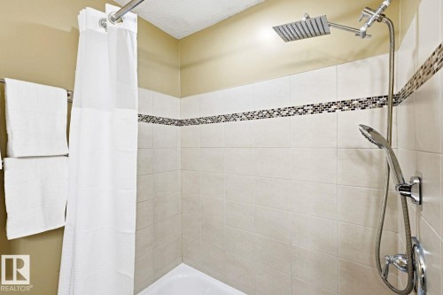 Tiled shower enclosure featuring a mosaic accent band, square rain shower head, and an additional handheld shower fixture - 11317 22 Avenue Nw, Edmonton, AB 