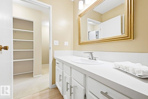 Vanity featuring an integrated sink, polished chrome faucet, white cabinetry with silver-tone hardware, and a framed mirror - 11317 22 Avenue Nw, Edmonton, AB 