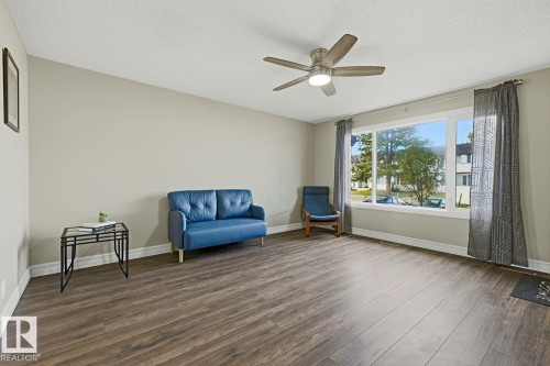 Spacious room featuring wood-finish flooring, a large picture window, and a ceiling fan with integrated lighting - 11317 22 Avenue Nw, Edmonton, AB 