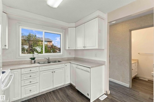White cabinetry with chrome hardware, dual-basin stainless steel sink, light-toned countertops, dishwasher, and wood-finish flooring - 17351 85 Avenue Nw, Edmonton, AB 