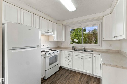 Kitchen featuring white cabinetry, wood-finish flooring, a double basin sink, and a large window - 17351 85 Avenue Nw, Edmonton, AB 
