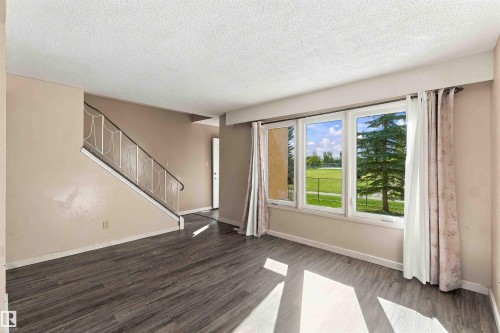 Wood-finish flooring, staircase with metal railing, three large windows, and neutral wall tones - 17351 85 Avenue Nw, Edmonton, AB 