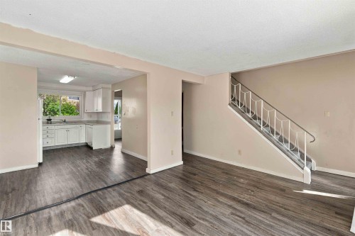 Wood-finish flooring throughout, white kitchen cabinetry, stainless steel sink, large window, and staircase with decorative railing - 17351 85 Avenue Nw, Edmonton, AB 