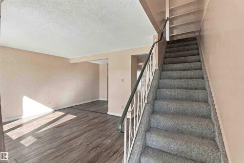 Wood-finish flooring and textured walls enhance the living area, while a carpeted staircase with a decorative metal railing leads to upper levels - 17351 85 Avenue Nw, Edmonton, AB 