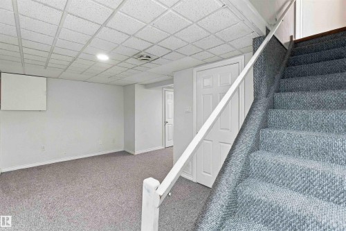 Gray carpeted flooring, white painted walls, white paneled doors, drop ceiling with recessed lighting, and white handrail - 17351 85 Avenue Nw, Edmonton, AB 