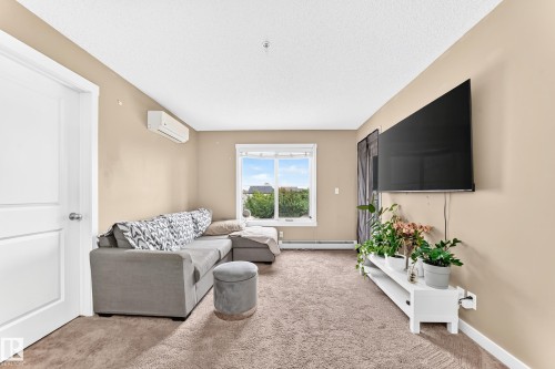 Wall-mounted air conditioning unit, window with exterior scenery, wall-mounted television, and neutral-toned carpeting - #306 5370 Chappelle Rd Sw, Edmonton, AB 